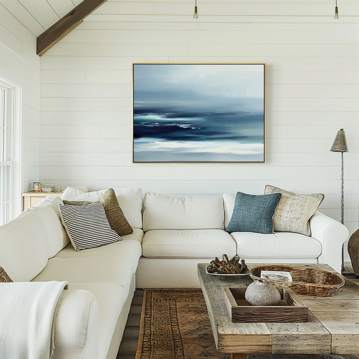 A bright, cozy living room features a white sectional sofa, blue and beige pillows, rustic coffee table, neutral decor, and the Sapphire Current Canvas Art - Horizontal on white shiplap walls. Sunlight pours in from a window.