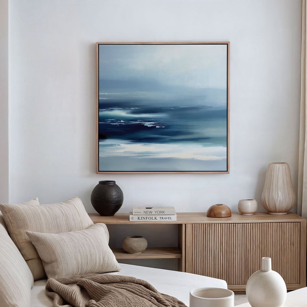 A modern, minimalist living room featuring a beige sofa, textured cushions, a wooden sideboard with decorative vases and books, and the Sapphire Current Canvas Art - Square on the white wall brings a touch of Nordic Park serenity.