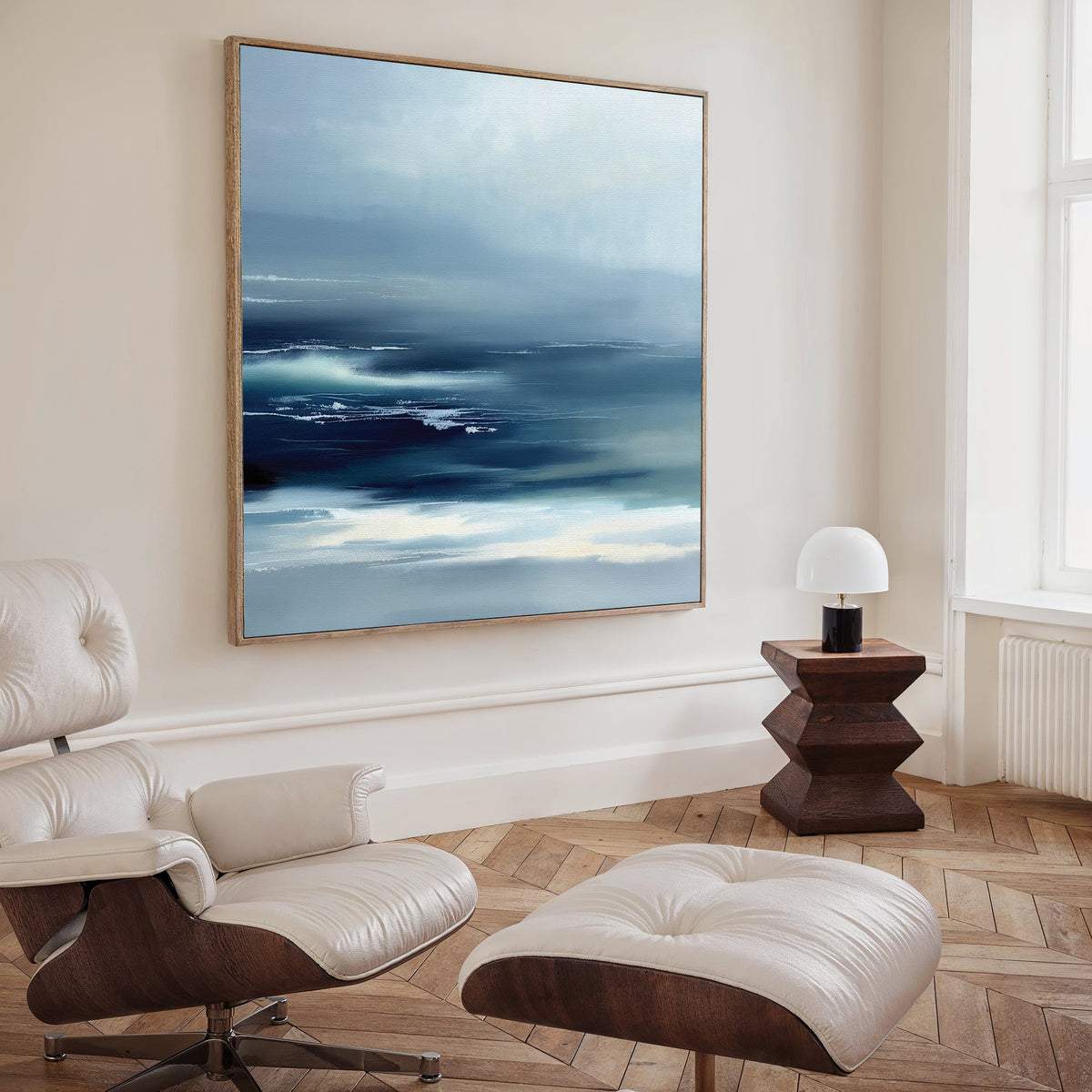 A modern living room features a cream lounge chair and ottoman, wooden side table with a white lamp, and the Sapphire Current Canvas Art - Square as tranquil wall art above, adding elegance to the serene space.
