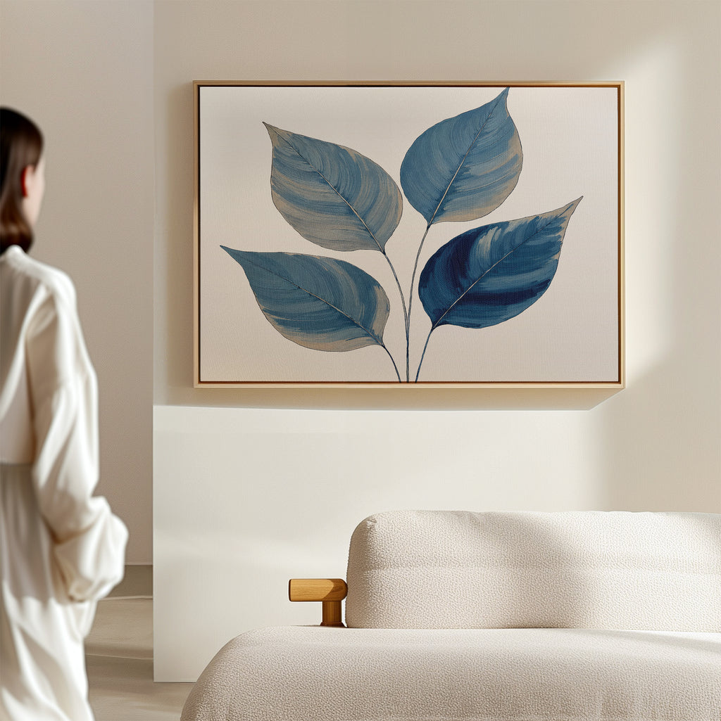 A person in white stands in a minimalist room, admiring the Sapphire Leaves Canvas Art - Horizontal. In front is a light sofa with wooden armrest, perfectly complementing the tranquil, botanical vibe of the blue leaf wall art.