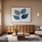 A modern living room features a light wood sideboard, beige sofa, wooden coffee table with a vase, and the Sapphire Leaves Canvas Art - Horizontal adding vibrant color above the sofa, all bathed in soft natural light from the window.