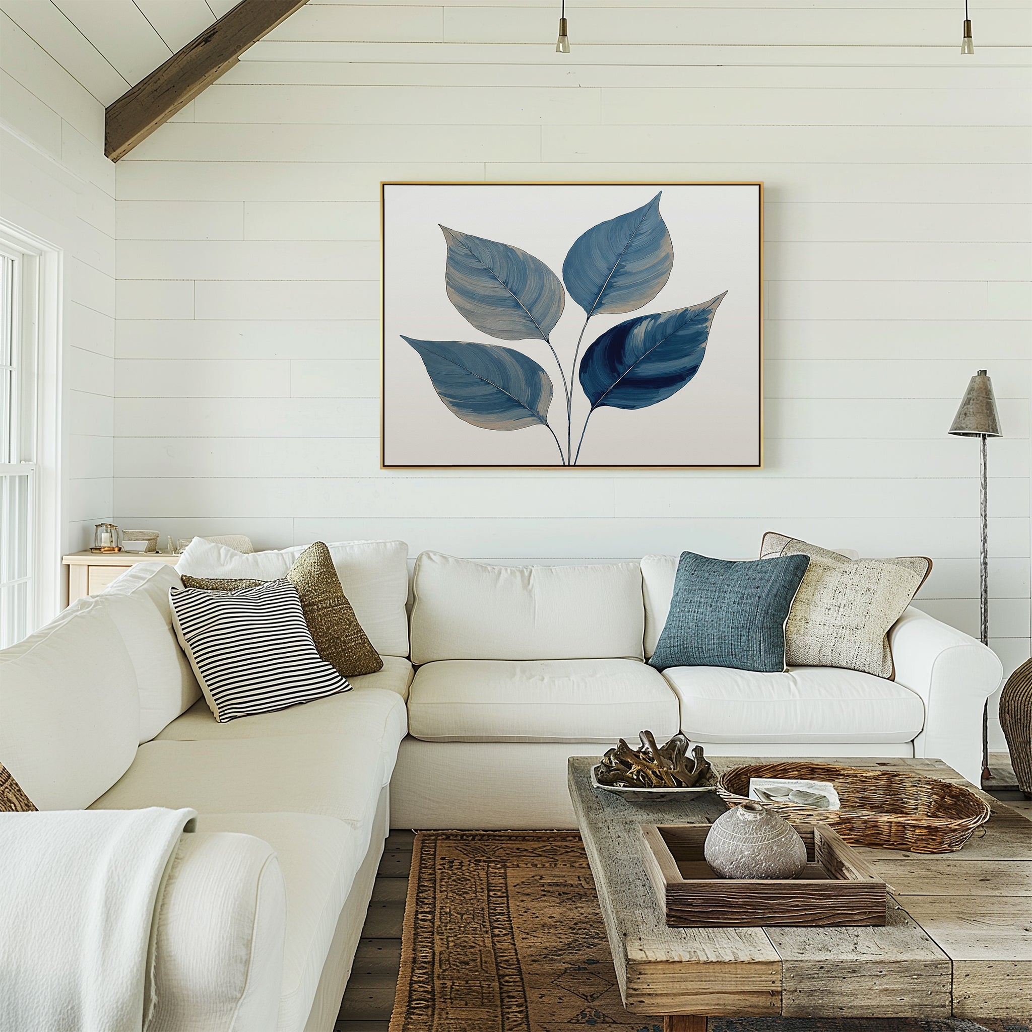 A bright, cozy living room features a white sectional sofa with assorted throw pillows, a wooden coffee table, and the Sapphire Leaves Canvas Art - Horizontal on a white shiplap wall. Natural light streams in from the left.