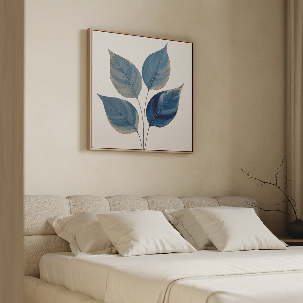 A minimalist bedroom with a beige bed, white pillows, and the Sapphire Leaves Canvas Art - Square showcasing blue botanical foliage above the headboard. A bare decorative branch rests on the bedside table.
