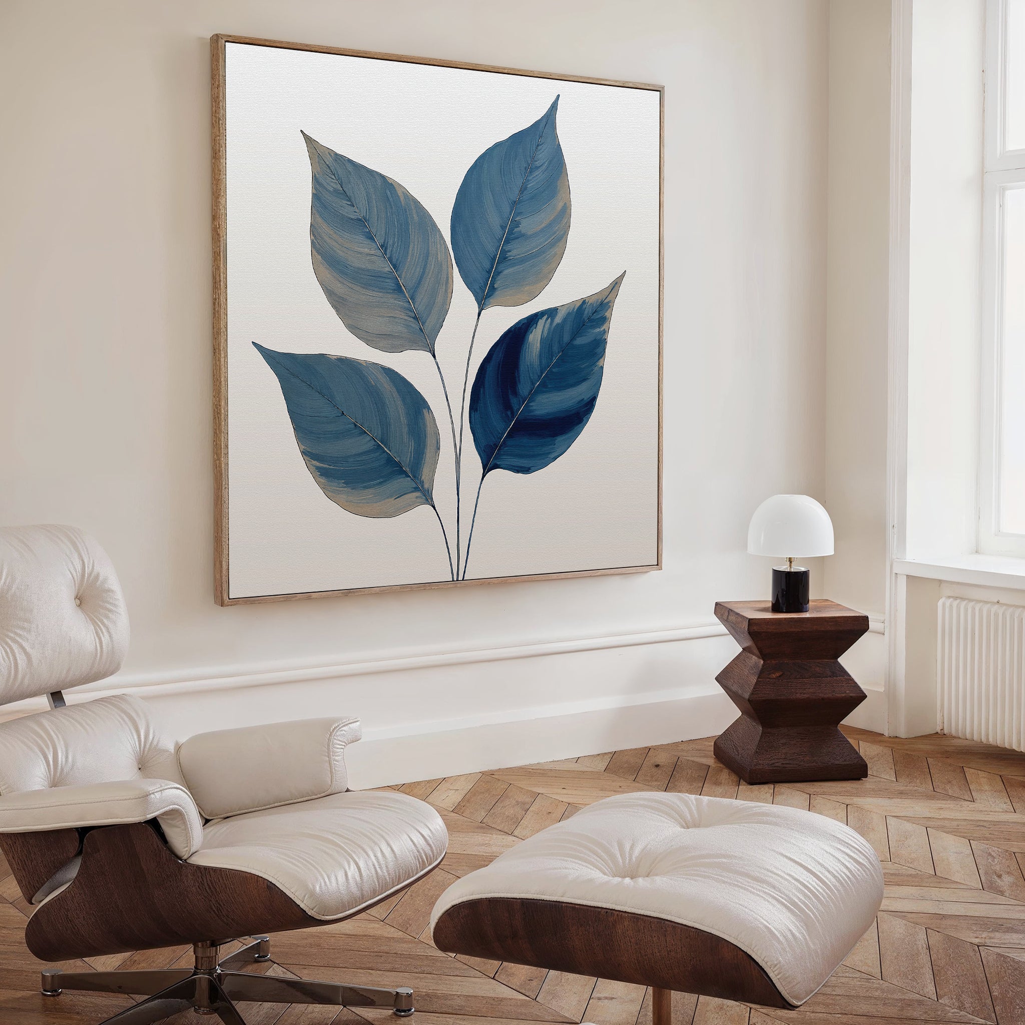 A modern living room features a white lounge chair and ottoman, wooden parquet floor, small dark wood side table with a round lamp, and the striking Sapphire Leaves Canvas Art - Square as wall decor.