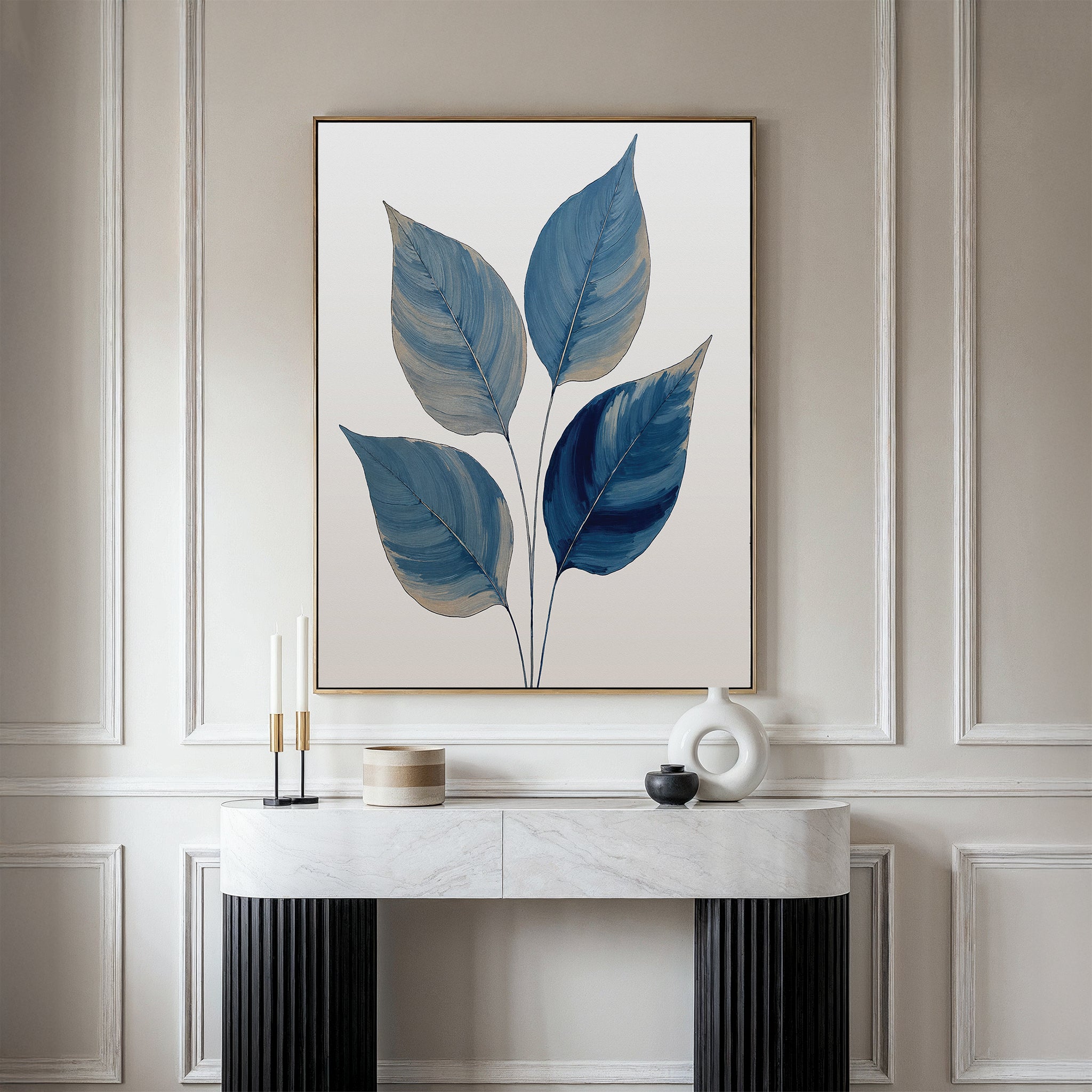 A modern room features calming blue wall art—a Sapphire Leaves Canvas Art - Vertical displayed above a white marble console table, which holds decorative objects like candles, a round sculpture, and a lidded container.