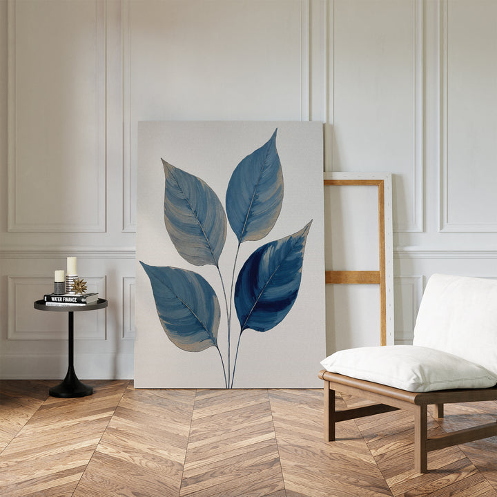 A modern room with white paneled walls, herringbone wood floor, a cushioned chair, round black side table with candles and books, and the calming Sapphire Leaves Canvas Art - Vertical botanical print resting against the wall.