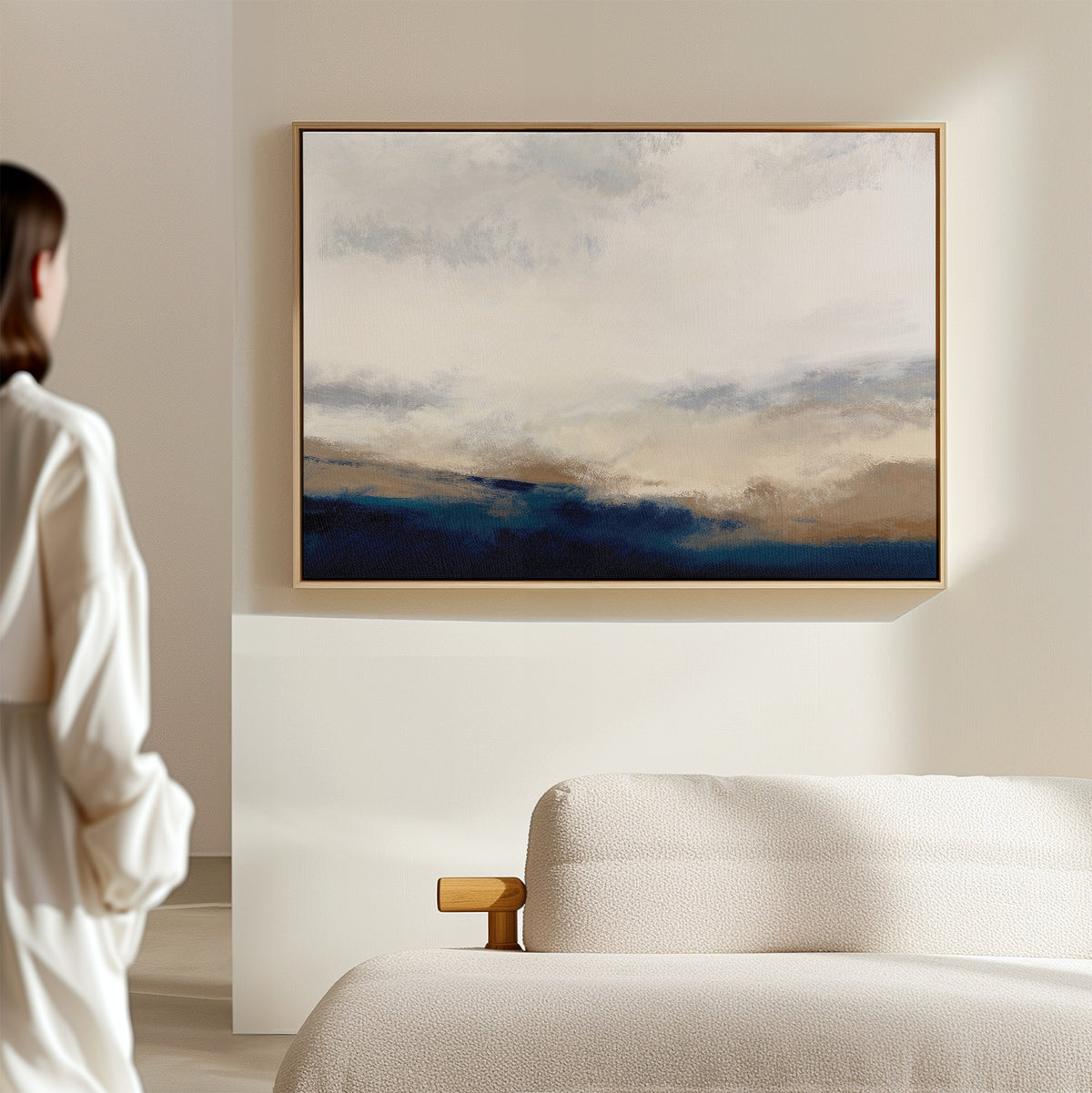 A person in a white shirt stands by a beige sofa, admiring the Sapphire Tides Canvas Art - Horizontal, a framed abstract print with cobalt blue and beige tones that adds modern wall decor to the light-colored room.
