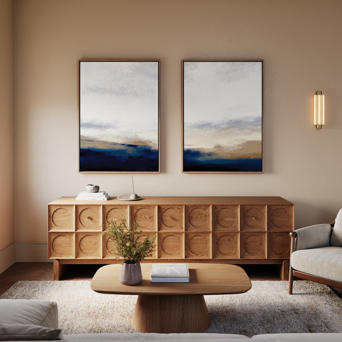 A modern living room featuring a wooden credenza, the Sapphire Tides - Set Of 2 abstract prints above it, a light wood coffee table with a vase, and a light-colored sofa. Soft lighting and cobalt blue accents create cozy, contemporary charm.