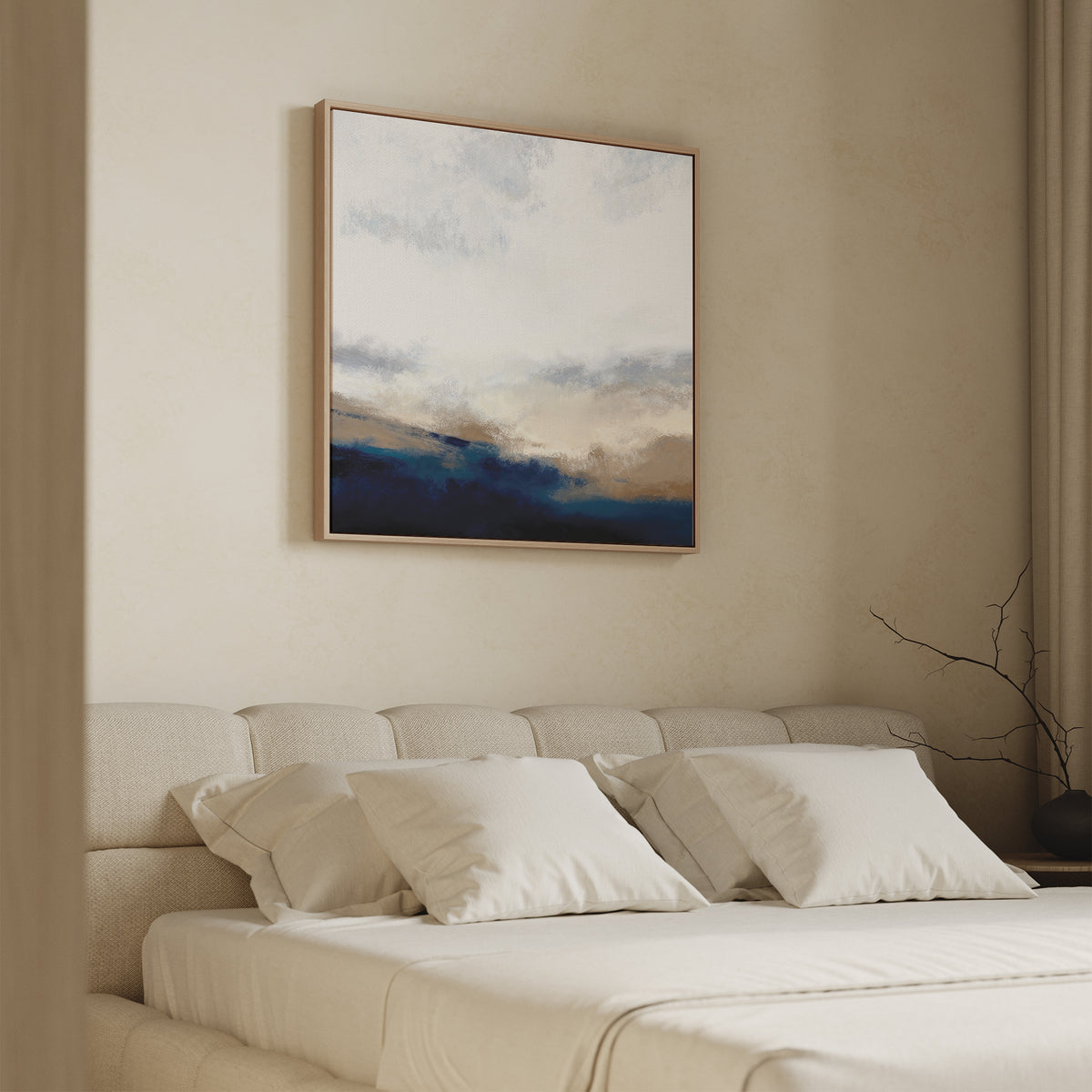 A modern, minimal bedroom features a beige bed, cream bedding, and neutral walls. Above the bed hangs the Sapphire Tides Canvas Art - Square with cobalt blue, brown, and white tones. A bare twig decorates the side table.