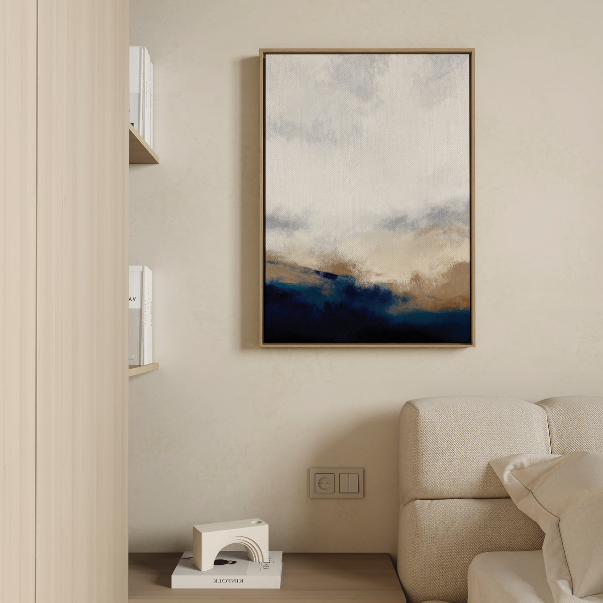 A modern living room features beige walls, a cream sofa, and the Sapphire Tides Canvas Art - Vertical in cobalt blue and tan hues. A shelf displays books and a white geometric decor piece.