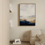 A modern living room features beige walls, a cream sofa, and the Sapphire Tides Canvas Art - Vertical in cobalt blue and tan hues. A shelf displays books and a white geometric decor piece.