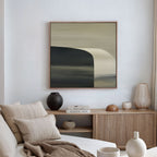 A modern living room with minimalist decor features a beige sofa and cushions, a wooden sideboard topped with books and vases, and the Sculptural Forms Canvas Art - Square in neutral tones hanging on the wall.