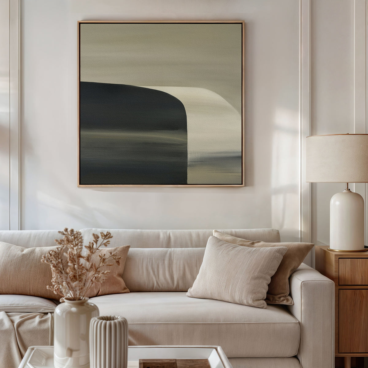 A modern living room with minimalist decor: a light beige sofa, neutral throw pillows, a wooden side table topped with a ceramic lamp and dried flowers, and the Sculptural Forms Canvas Art - Square displayed on the wall.