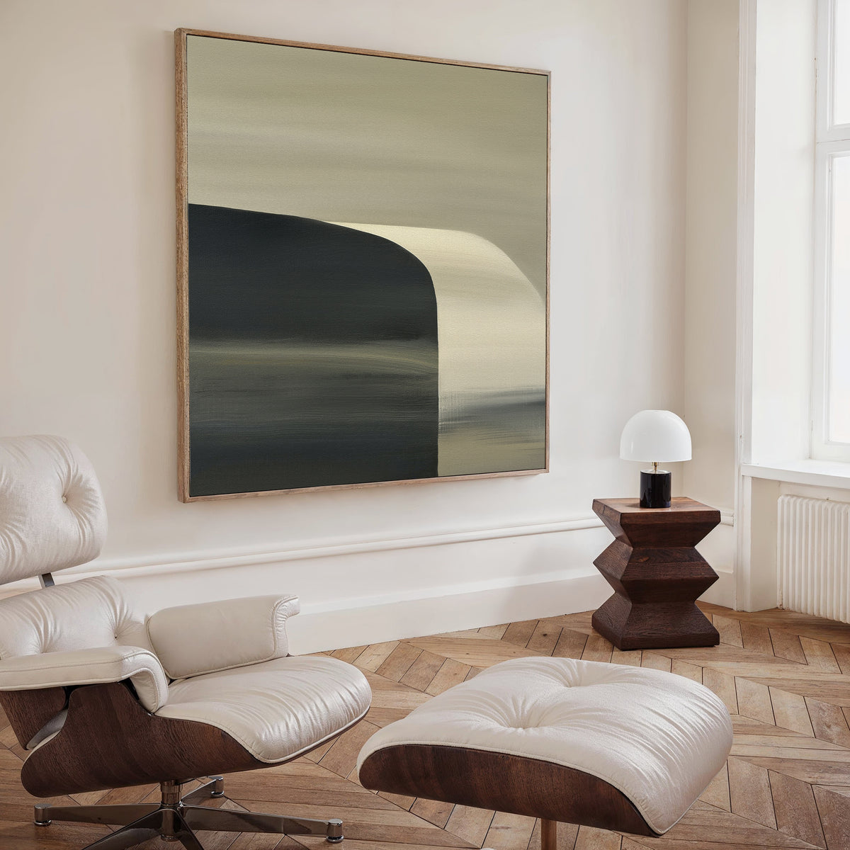 A modern, minimalist living room featuring a white leather lounge chair and ottoman, a wooden side table with a small white lamp, chevron-patterned wood floors, and the Sculptural Forms Canvas Art - Square in neutral tones on the wall.