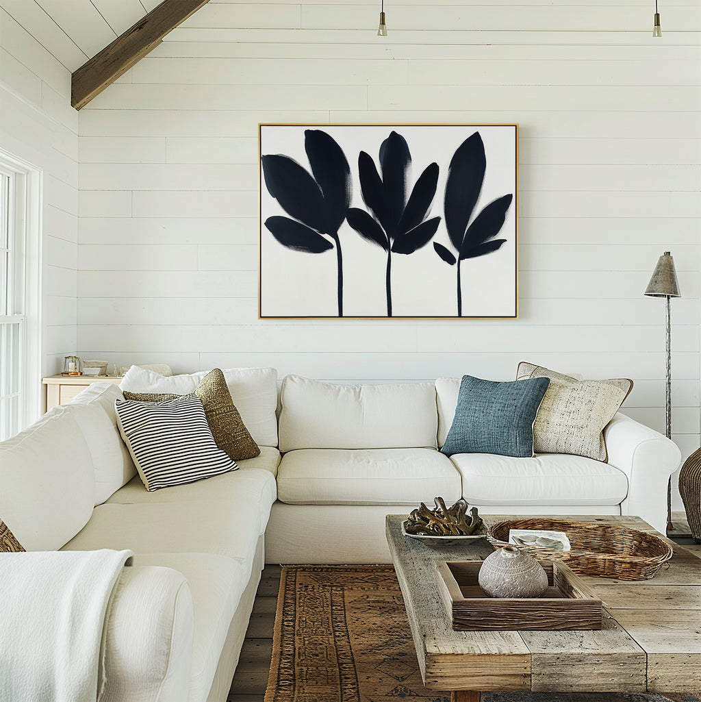 A cozy living room with a white sectional, assorted pillows, a wood coffee table with décor, and the Shadow Stems Canvas Art - Horizontal on a white shiplap wall—an ideal modern accent.