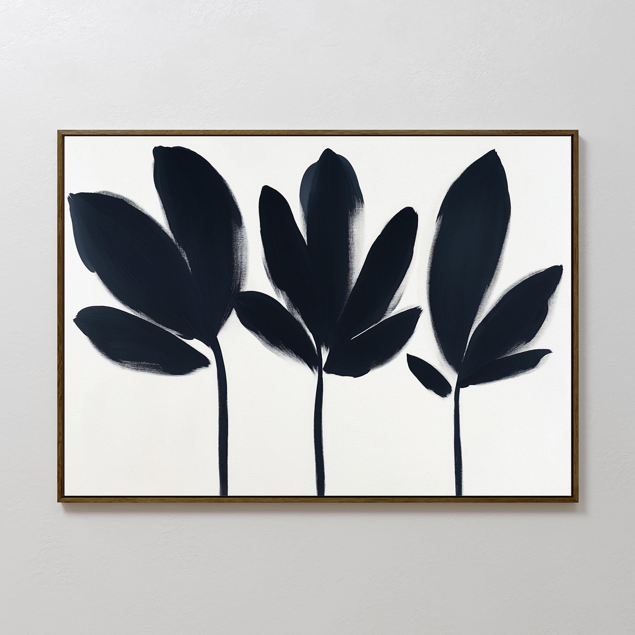 Shadow Stems Canvas Art - Horizontal features three black botanical silhouettes with stems on a white background, framed in a slim dark brown frame. Its simple, modern style is ideal for contemporary living rooms.