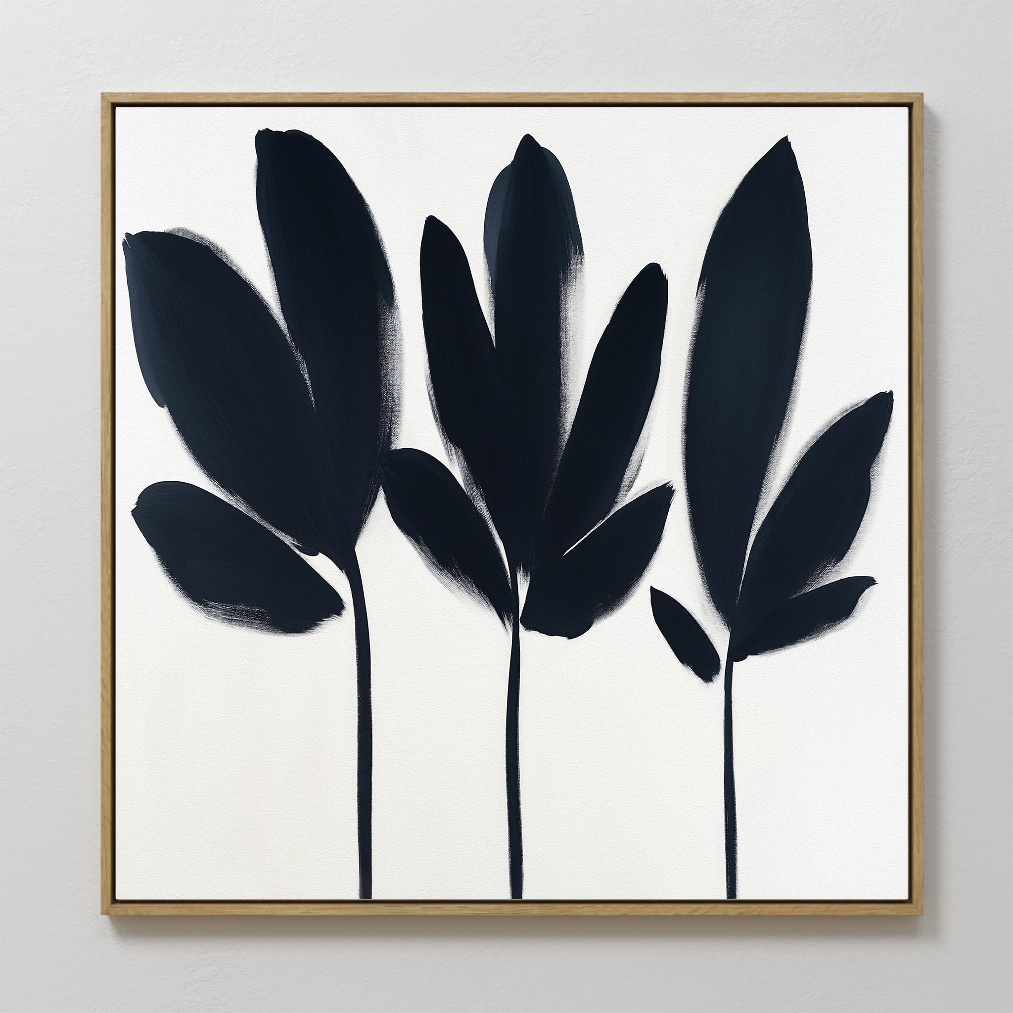 The Shadow Stems Canvas Art - Square features three abstract black leafy silhouettes with long stems on white, framed in light wood. Bold brushstrokes add a modern touch, ideal for contemporary living rooms.