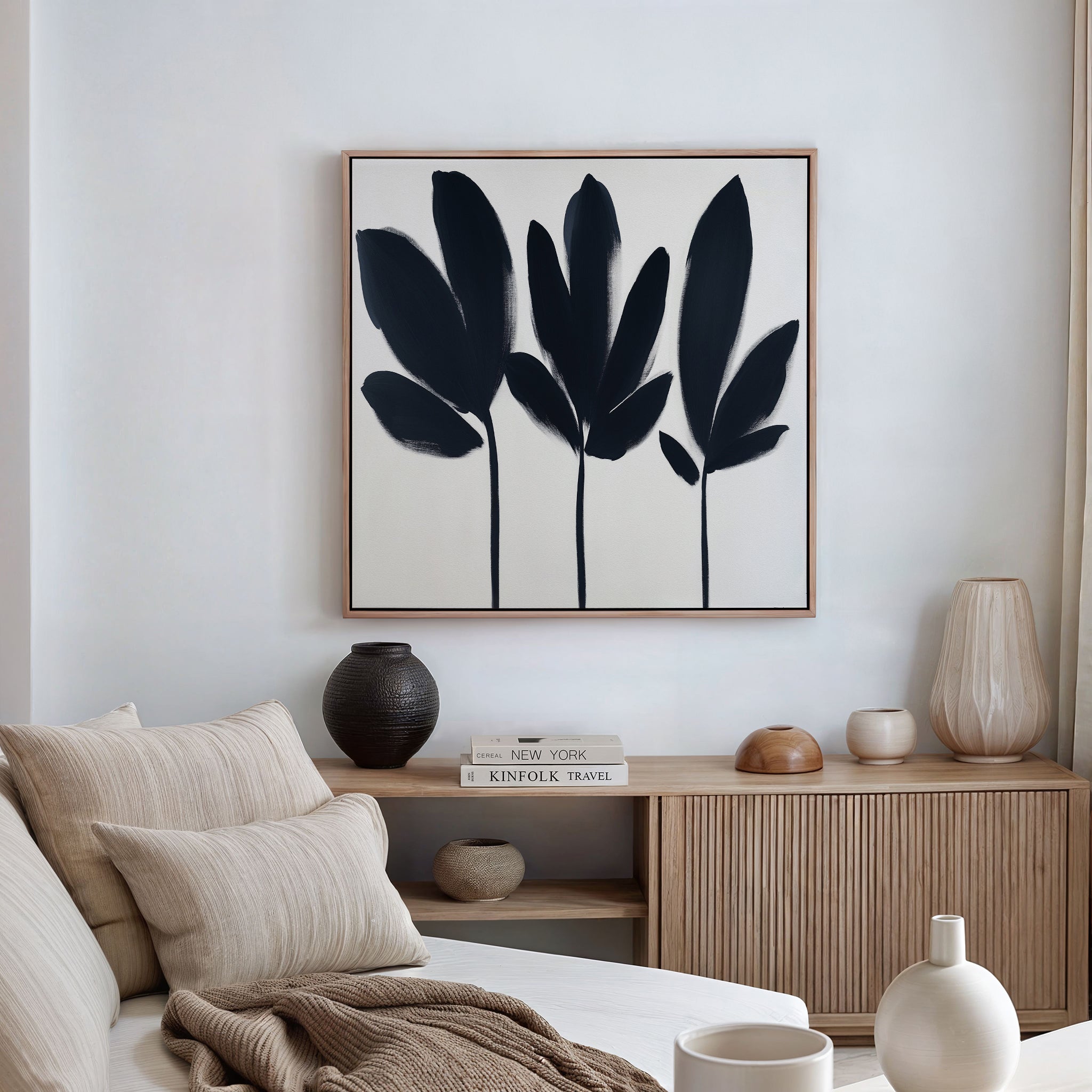 A modern, minimalist living room with a beige sofa, neutral cushions, wooden sideboard, ceramic vases, and the Shadow Stems Canvas Art - Square featuring botanical silhouettes displayed above the sideboard.