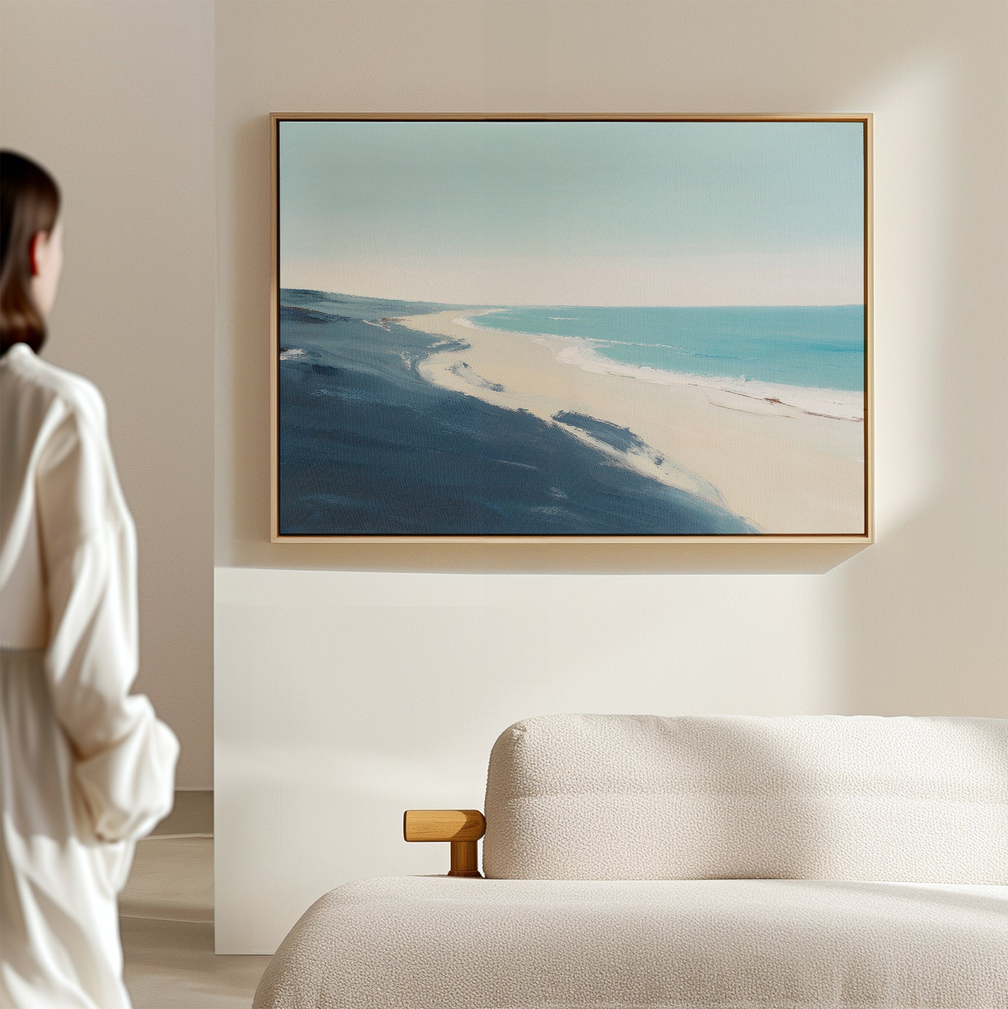 A woman in a white shirt stands in a bright, minimal room, admiring the Shifting Tides Canvas Art - Horizontal with blue and beige tones, displayed above a beige upholstered bed.