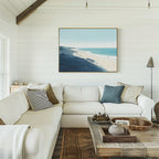A cozy living room features a white sectional, assorted pillows, rustic wooden coffee table, and the Shifting Tides Canvas Art - Horizontal on a white shiplap wall, with natural light streaming in from a left window.