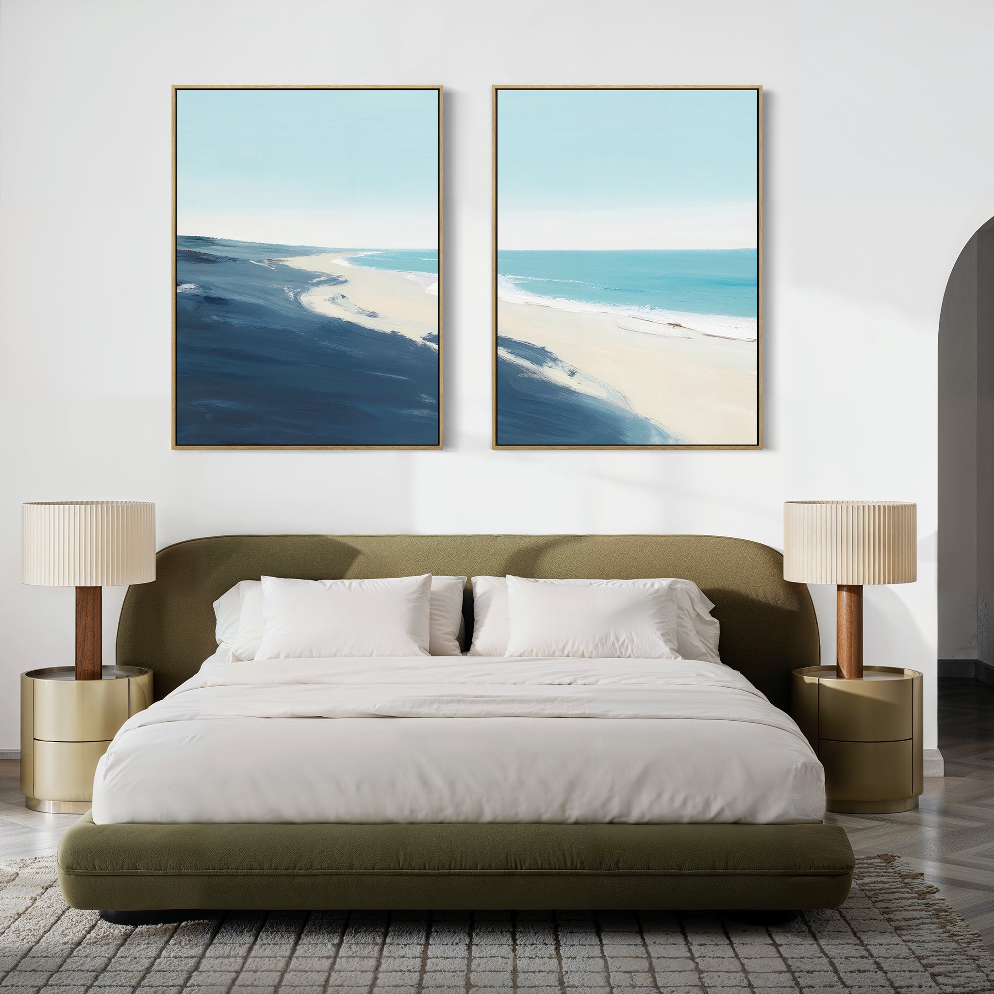 A modern bedroom features a green upholstered bed with white bedding, beige nightstands and lamps, and "Shifting Tides - Set of 2" seaside wall art depicting a beach scene above the bed.