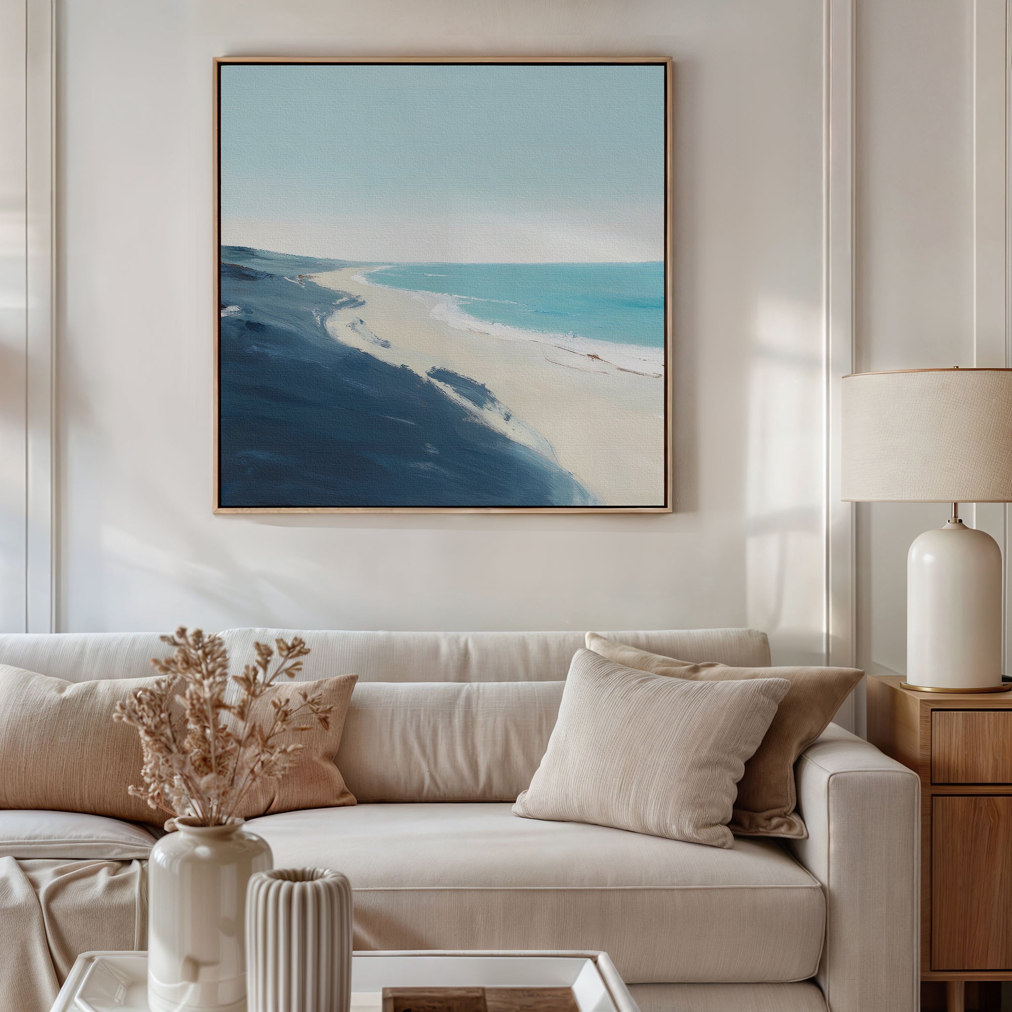 A bright, modern living room featuring a beige sofa, neutral cushions, a dried floral arrangement in a vase, table lamp, and the Shifting Tides Canvas Art - Square adds relaxed elegance to this Nordic Park-inspired space.