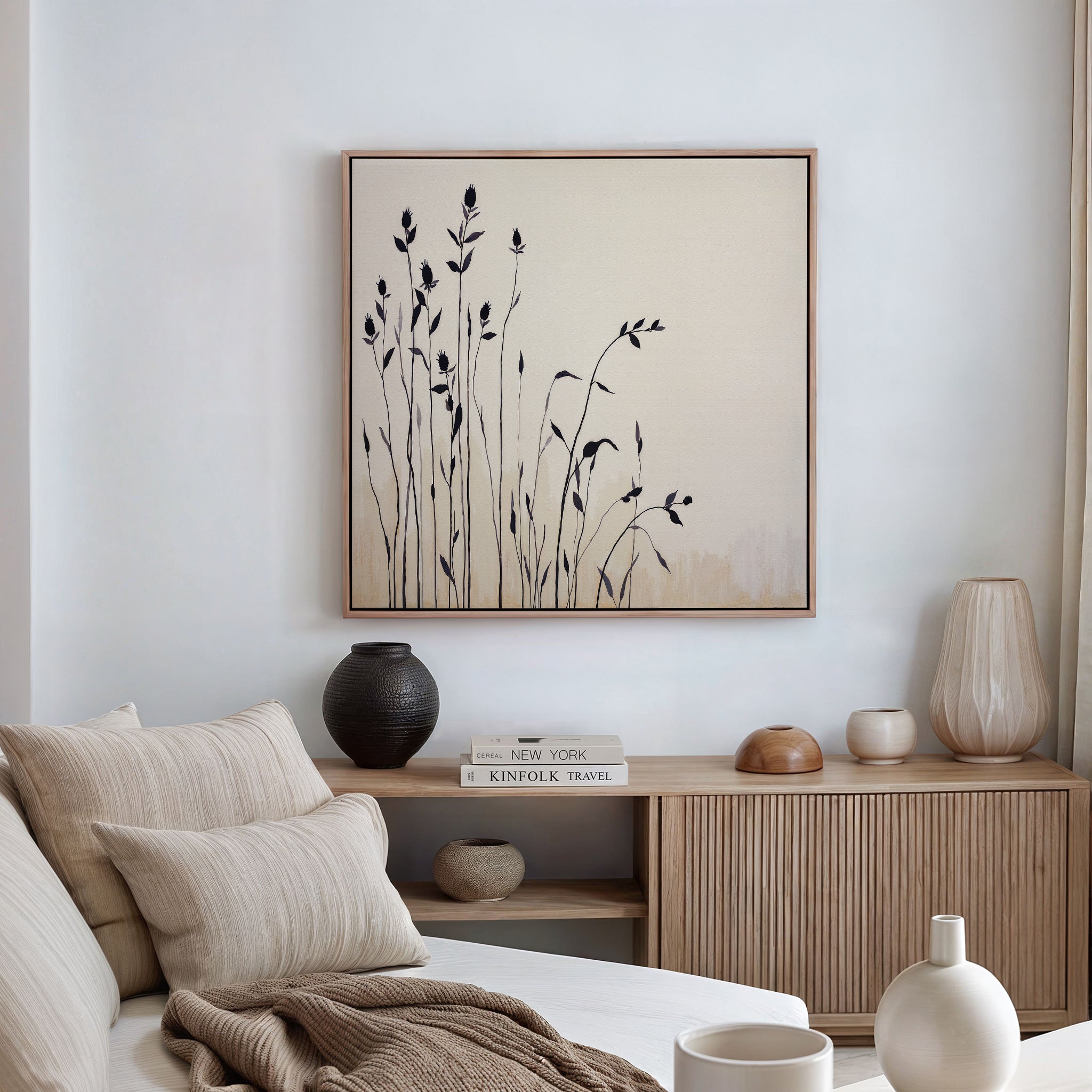 A minimalist living room with a beige sofa and wooden sideboard displays vases and books, featuring the Silhouette Meadow Canvas Art - Square above for a touch of Nordic decor.