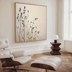 A modern living room features a white leather lounge chair and ottoman, a dark wood side table with a white lamp, and the Silhouette Meadow Canvas Art - Square—an elegant complement to minimalist Nordic decor.