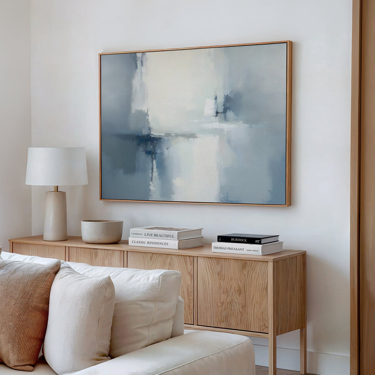 A minimalist living room features a light wood sideboard with decor and a white lamp. Above the cream sofa hangs the Silver Cross Formation Canvas Art - Horizontal, adding modern flair to the space.