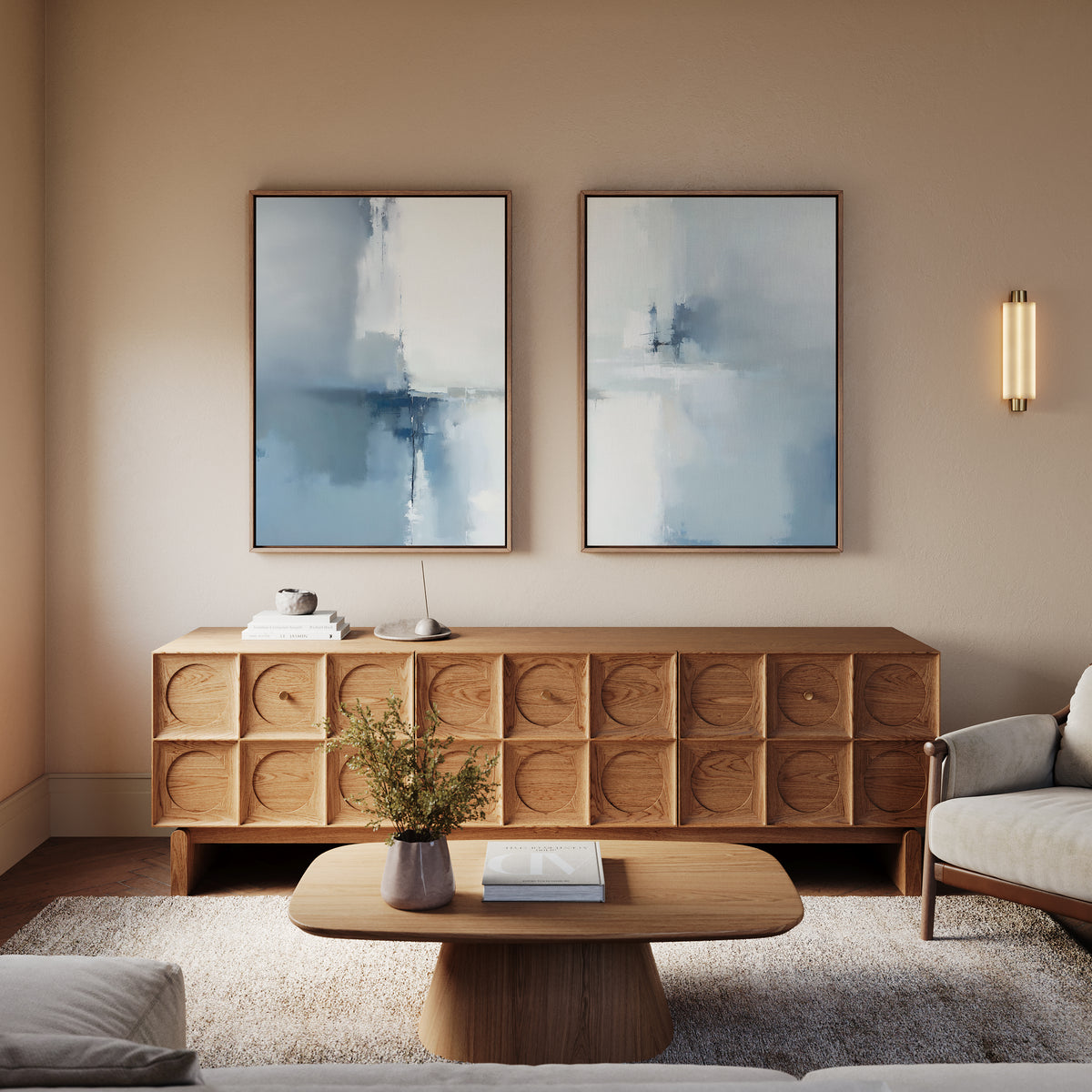 A modern living room features a wooden sideboard, the Silver Cross Formation - Set Of 2 artwork prints above it, a wooden coffee table with books, a beige sofa, and a wall sconce—all in neutral tones.