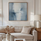 A modern living room featuring a beige sofa, neutral cushions, a ceramic lamp, vases with dried flowers, and the Silver Cross Formation Canvas Art - Square in blue and white above the sofa for an atmospheric touch.