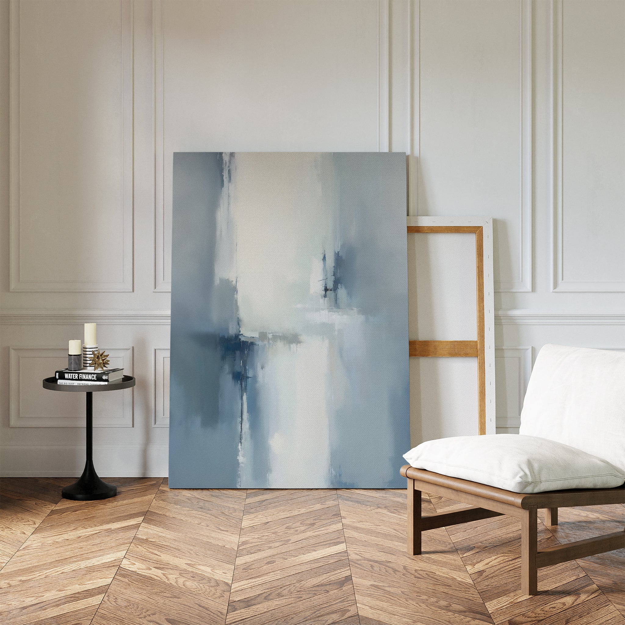 A minimalist living space with herringbone wood floors, a white cushioned chair, a round side table with candles and books, and the Silver Cross Formation Canvas Art - Vertical leaning against a white paneled wall—ideal for modern living rooms.