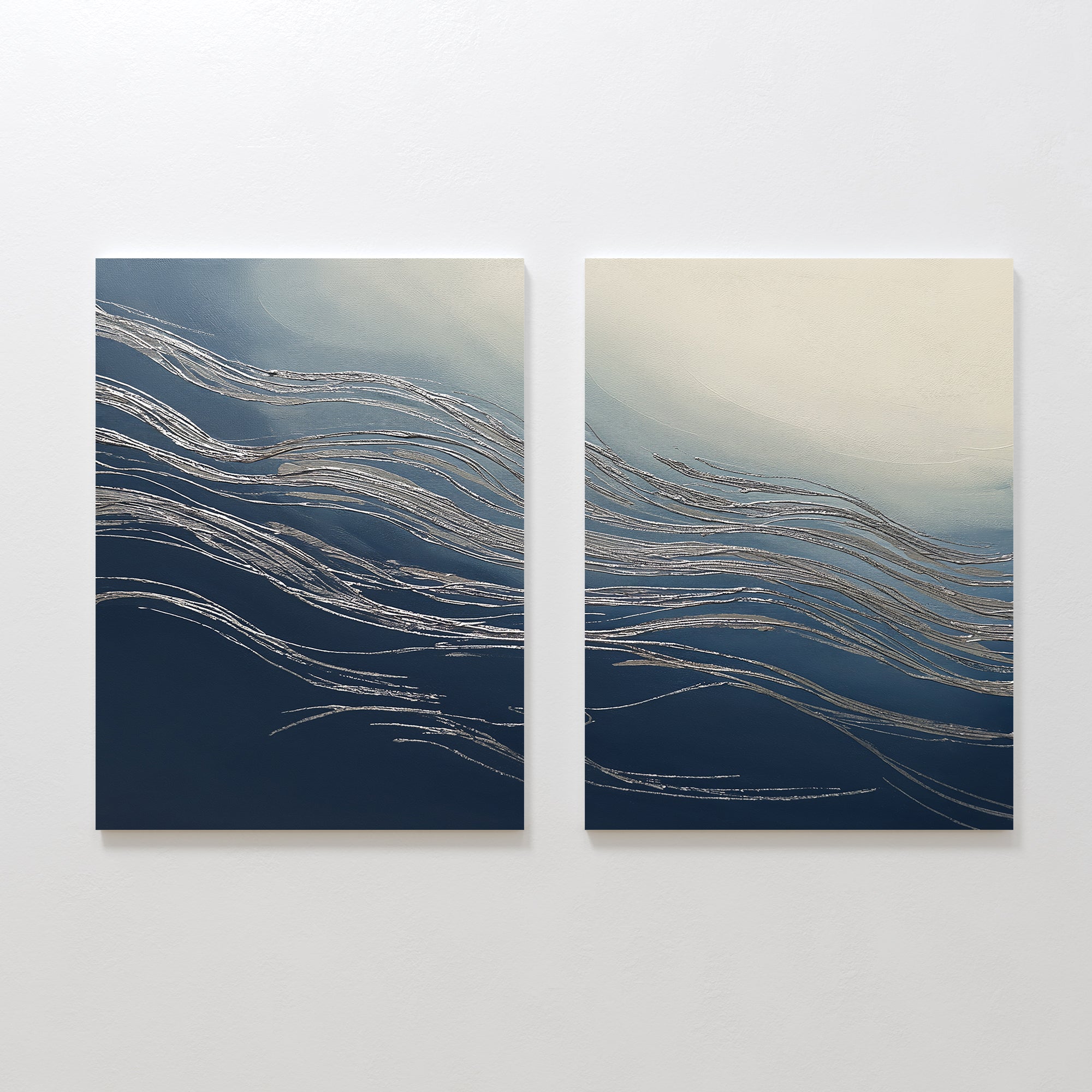 Silver Current - Set Of 2 features abstract canvas paintings with flowing silver lines on gradient blue and white backgrounds, evoking waves or wind. Hung side by side, they add contemporary sophistication to any space.