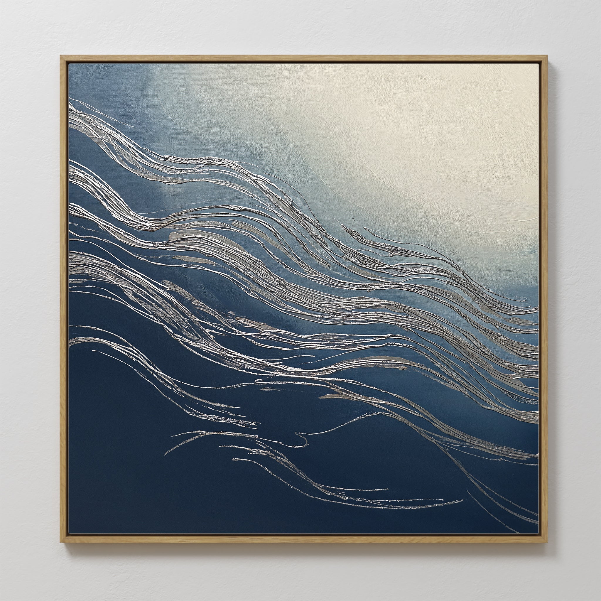 The Silver Current Canvas Art - Square features metallic silver wavy lines on a gradient blue and cream background, reminiscent of water currents. Framed in light wood, it adds a sophisticated contemporary touch to any white wall.