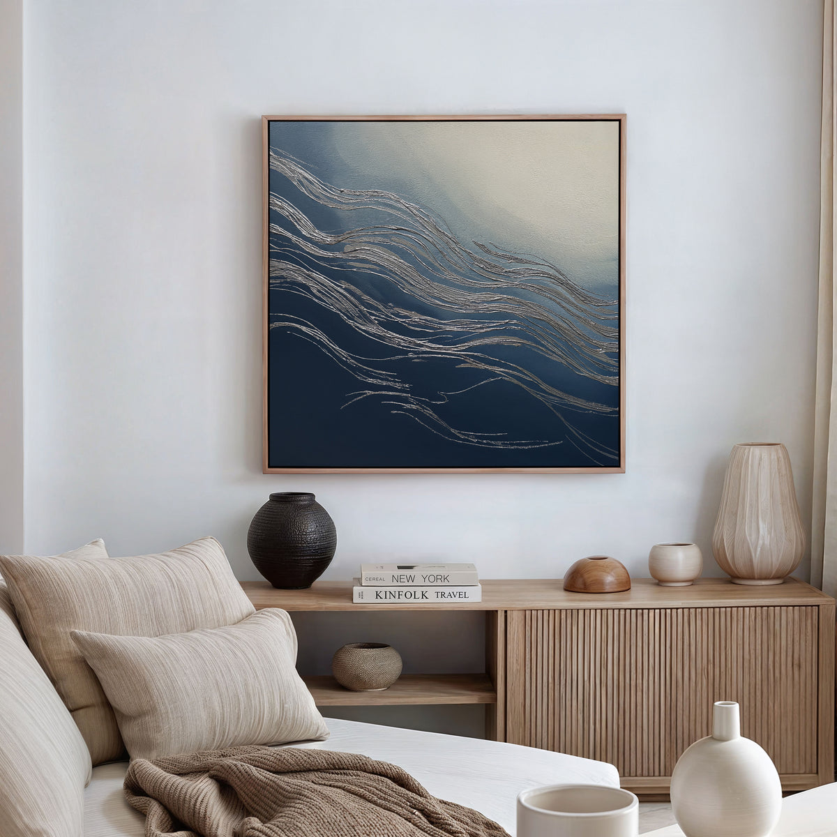 A modern living room with neutral furniture, a wooden sideboard, and decorative ceramics is enhanced by the Silver Current Canvas Art - Square, featuring wavy silver lines on blue and cream tones for a sophisticated contemporary touch.