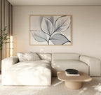 A modern living room features a light beige sectional, wooden coffee table with black bowl, neutral rug, tall plant, and the Silver Leaves Canvas Art - Horizontal on the cream wall. Perfect for modern decor lovers as sunlight softly filters in.