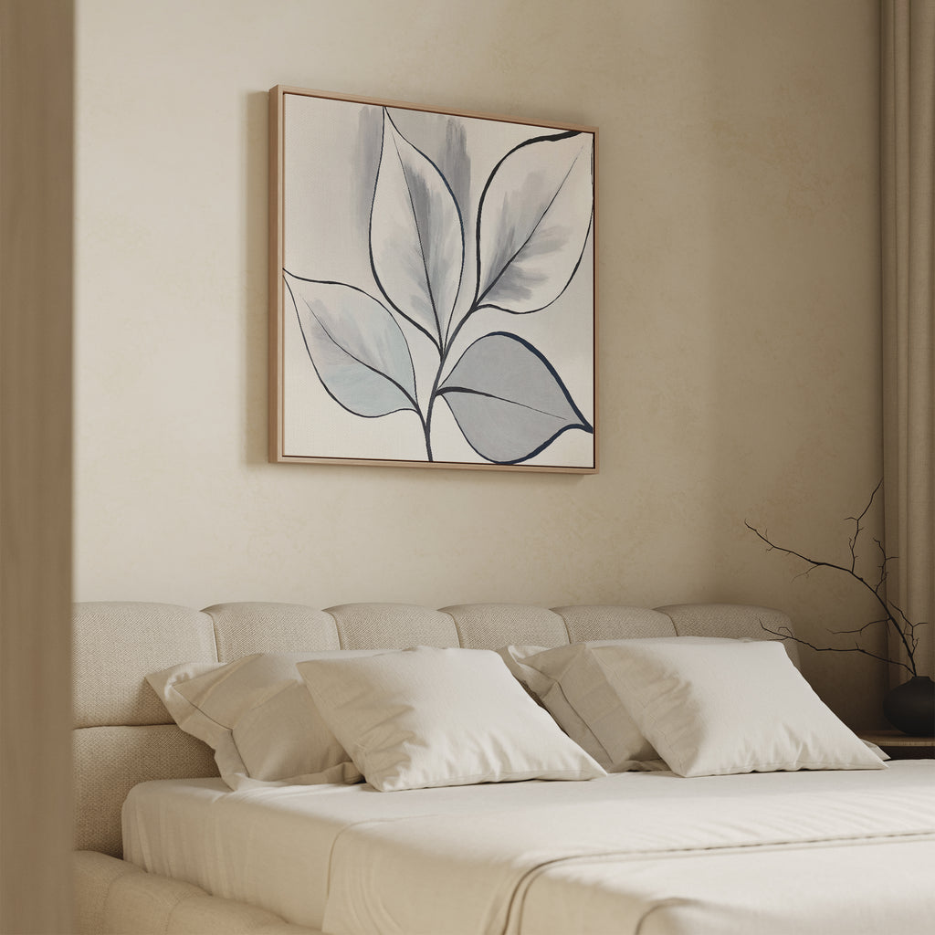 A minimal bedroom features a beige upholstered bed with white bedding and four pillows. Above the bed hangs the Silver Leaves Canvas Art - Square, while soft lighting and neutral tones create a calm, serene space for modern home decor.