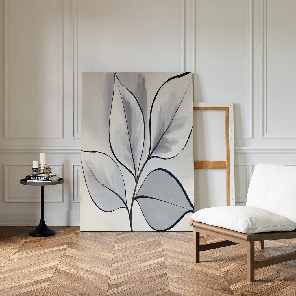 A minimalist room with herringbone wood floors, white paneled walls, a modern white chair, black round side table with candles, and the Silver Leaves Canvas Art - Vertical in muted tones leaning against the wall as decor.