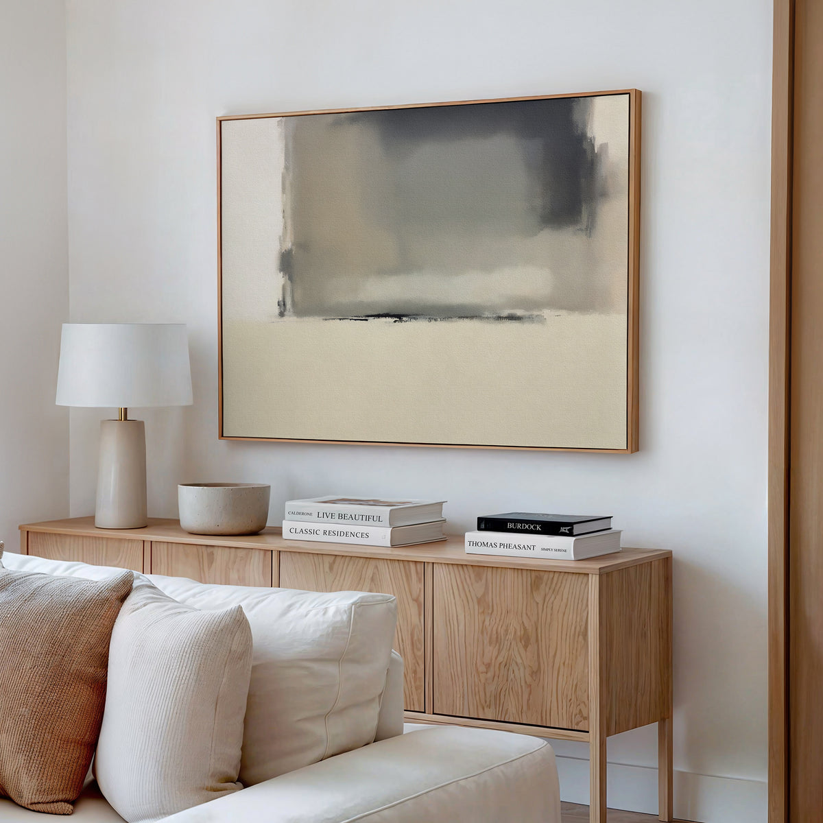 A modern living room with a light wood sideboard, stacked books, a white table lamp, and neutral decor. Above the sideboard on a crisp white wall hangs the Smoke Boundary Canvas Art - Horizontal in beige, gray, and black tones.