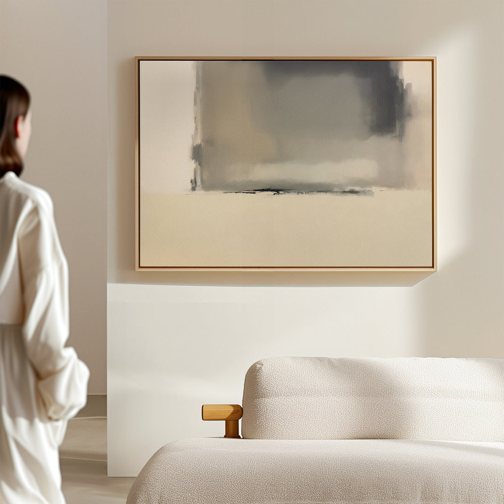 A person stands in a serene, minimalist room with a light-colored sofa and the Smoke Boundary Canvas Art - Horizontal, a striking abstract piece in soft neutral tones, displayed on the wall.