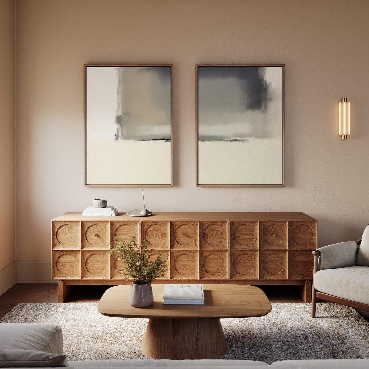 A modern living room featuring the Smoke Boundary - Set Of 2 wall art above a wooden sideboard, a wooden coffee table with a book and vase, a light-colored armchair, beige walls, and a wall sconce.