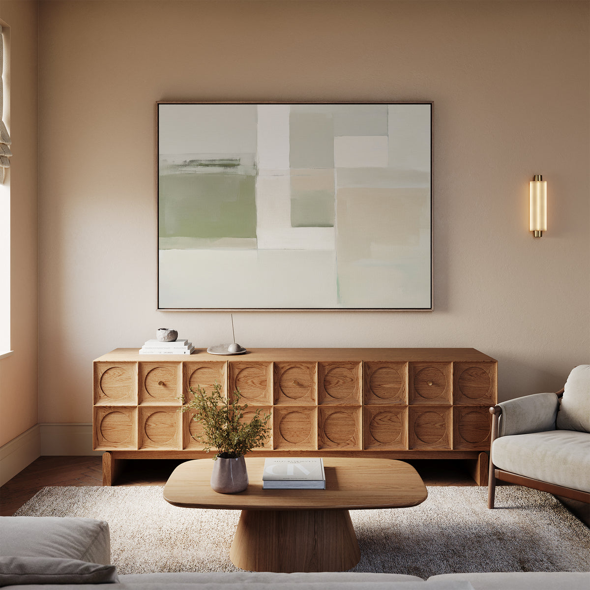 A modern living room featuring a wood sideboard, the Soft Geometric Planes Canvas Art - Horizontal, a round coffee table with books and flowers, a beige sofa, and neutral walls with soft lighting.