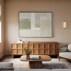 A modern living room featuring a wood sideboard, the Soft Geometric Planes Canvas Art - Horizontal, a round coffee table with books and flowers, a beige sofa, and neutral walls with soft lighting.