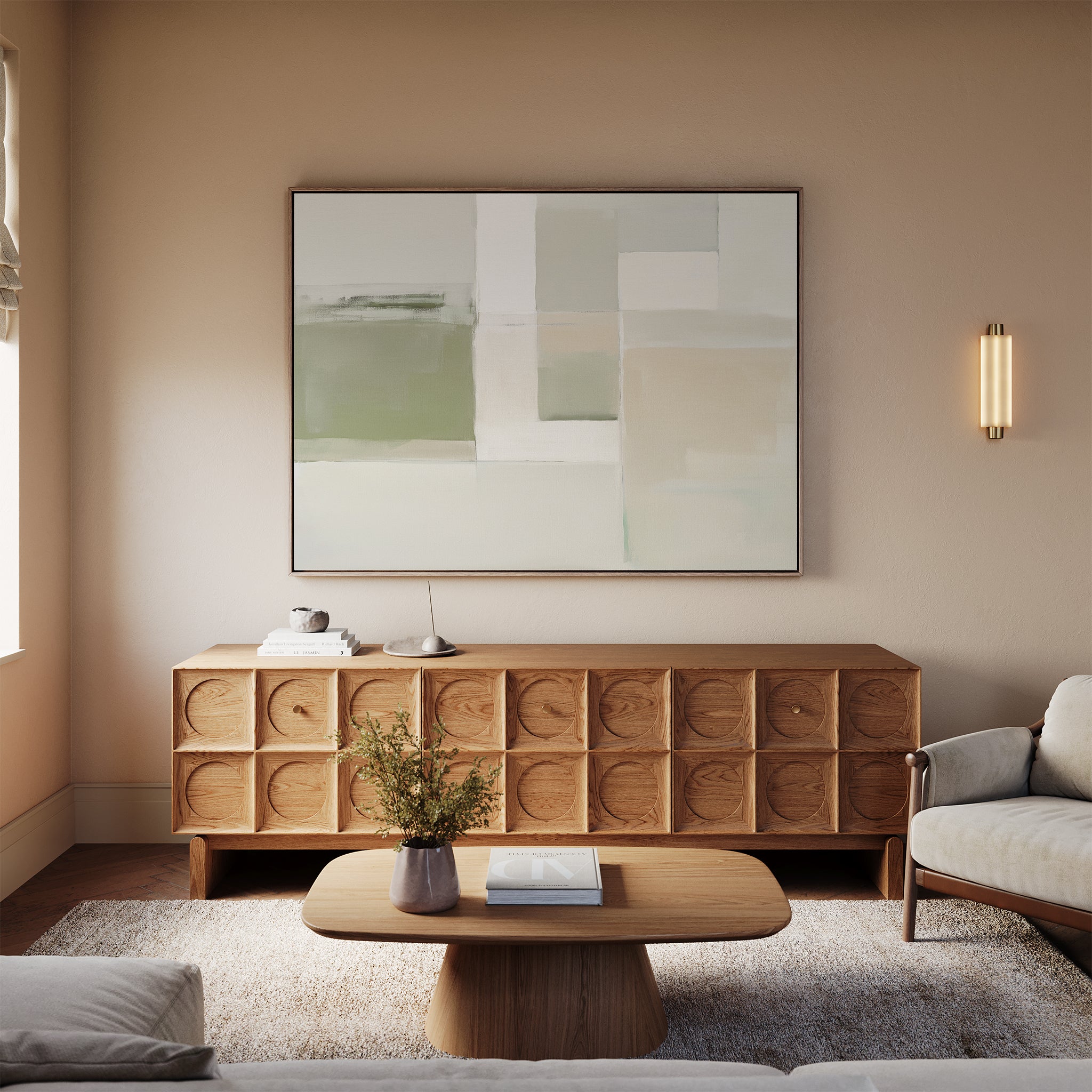 A modern living room featuring a wood sideboard, the Soft Geometric Planes Canvas Art - Horizontal, a round coffee table with books and flowers, a beige sofa, and neutral walls with soft lighting.