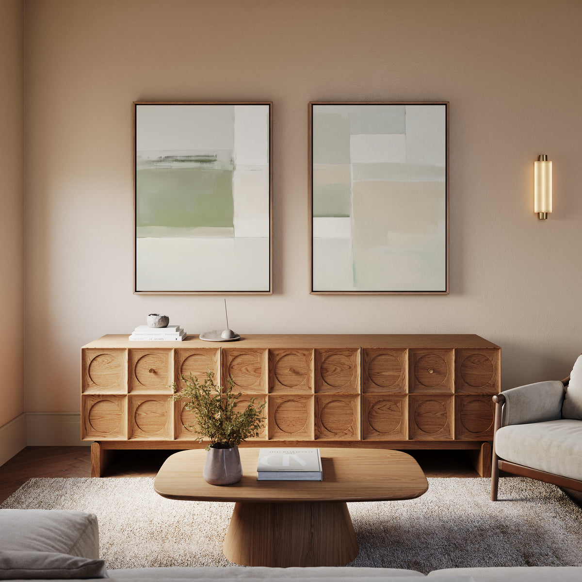 A modern living room featuring the Soft Geometric Planes - Set Of 2 wall art in green and beige, a wooden sideboard, round coffee table, vase with greenery, armchair, and wall sconce—all in neutral tones for chic decor.