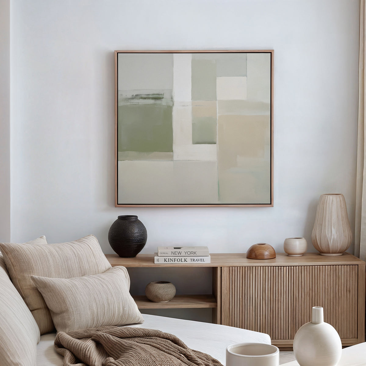 A minimalist living room featuring a beige sofa, cushions, a wooden sideboard with ceramics and books, and the Soft Geometric Planes Canvas Art - Square in soft neutral tones enhancing the contemporary feel on a white wall.