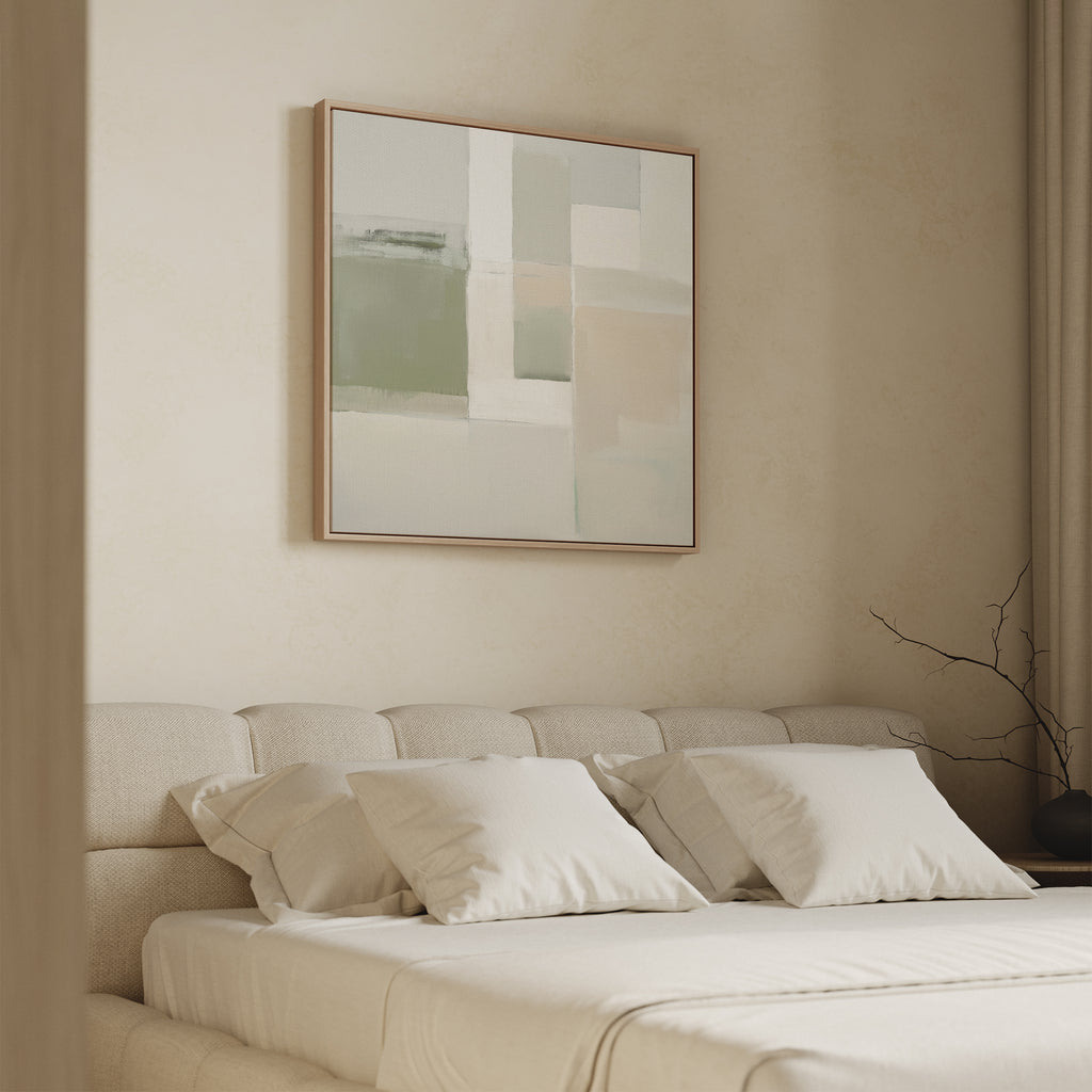 A minimalist bedroom features a beige bed, four white pillows, and the Soft Geometric Planes Canvas Art - Square in soft green and neutral tones above the headboard, plus a bare branch in a vase on the side table for a modern look.