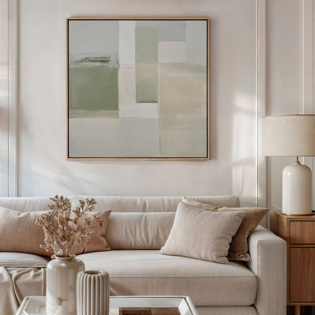 A modern living room featuring a beige sofa, neutral cushions, a wooden side table with a ceramic lamp, dried flowers in a vase, and the Soft Geometric Planes Canvas Art - Square on the wall as sunlight streams in.
