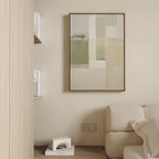 Minimalist living space with a beige wall, contemporary style, part of a light sofa, books on a small shelf, and the Soft Geometric Planes Canvas Art - Vertical featuring abstract green and cream tones as the focal point.