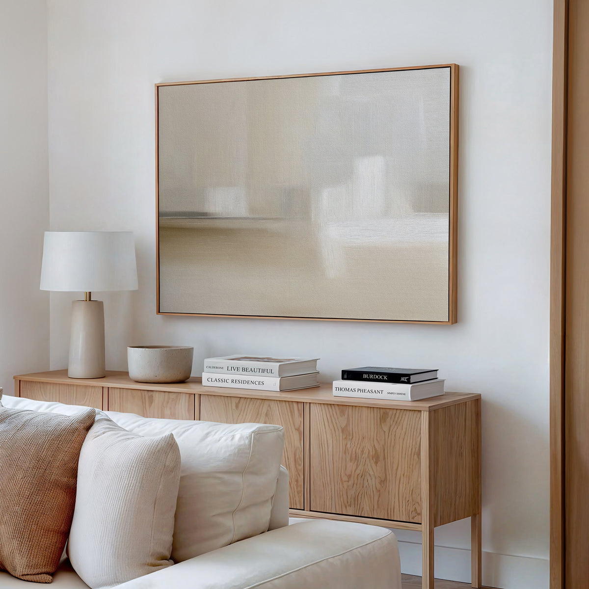 A minimalist living room with a light wood sideboard, books, lamp, beige sofa with cushions, and the Soft Layers Canvas Art - Horizontal in soft neutral tones enhancing the serene, neutral palette.